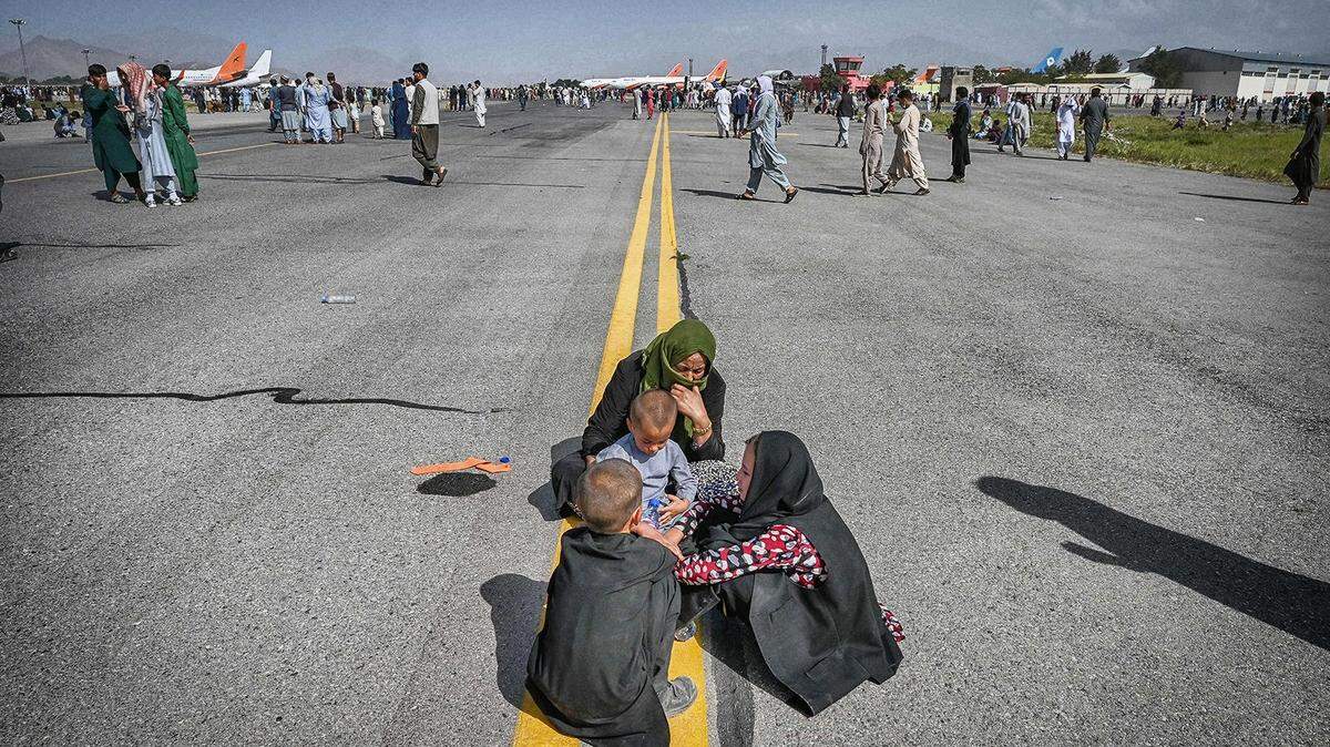 Afghans sit on the tarmac as they wait to leave the Kabul airport in Kabul, Afghanistan on Aug. 16, 2021, after a stunningly swift end to Afghanistan’s 20-year war.