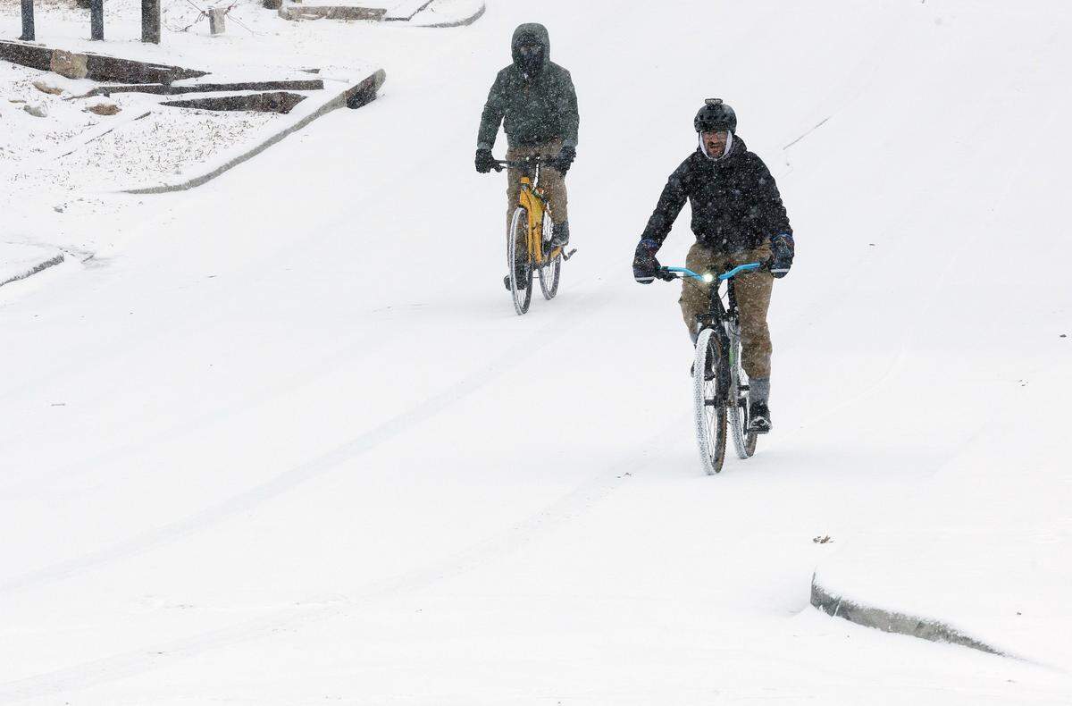 People ride bicycles as snow falls in downtown Durham on Saturday, Jan. 31, 2026.