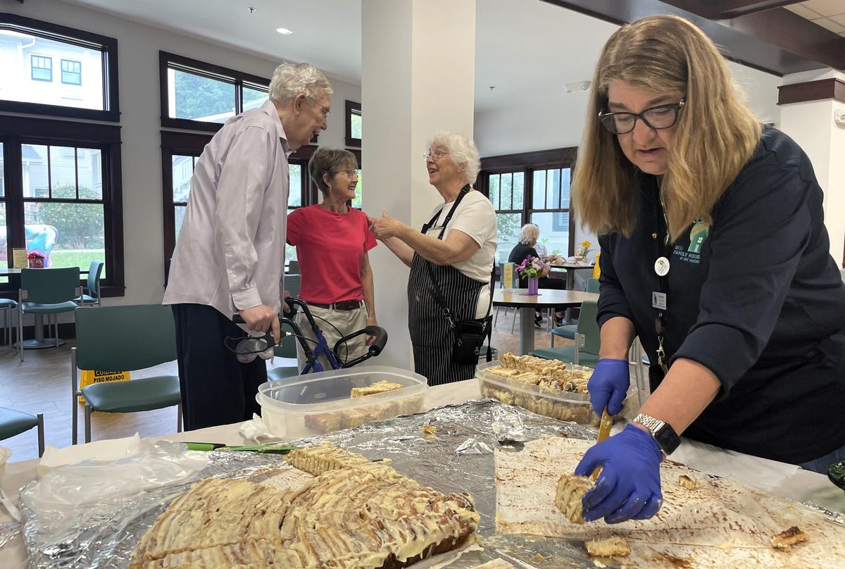 Asheville residents Don McNair and Cheryl Laughter chat with SECU Family House volunteer Donna Fehrenbach, center, as Georgie Clemens, right, director of Volunteer Services, slices up the remainder of a giant cinnamon roll Friday morning, Oct. 4, 2024.