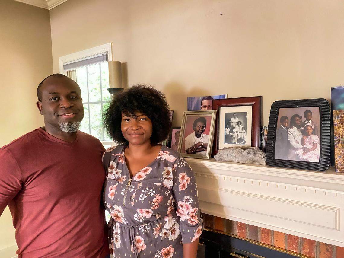 André Lafortune (left) and his wife Dafney Tales Lafortune (right) pose for a photo in front of portraits of their ancestors from Haiti at their home in Durham, North Carolina on July 18, 2021