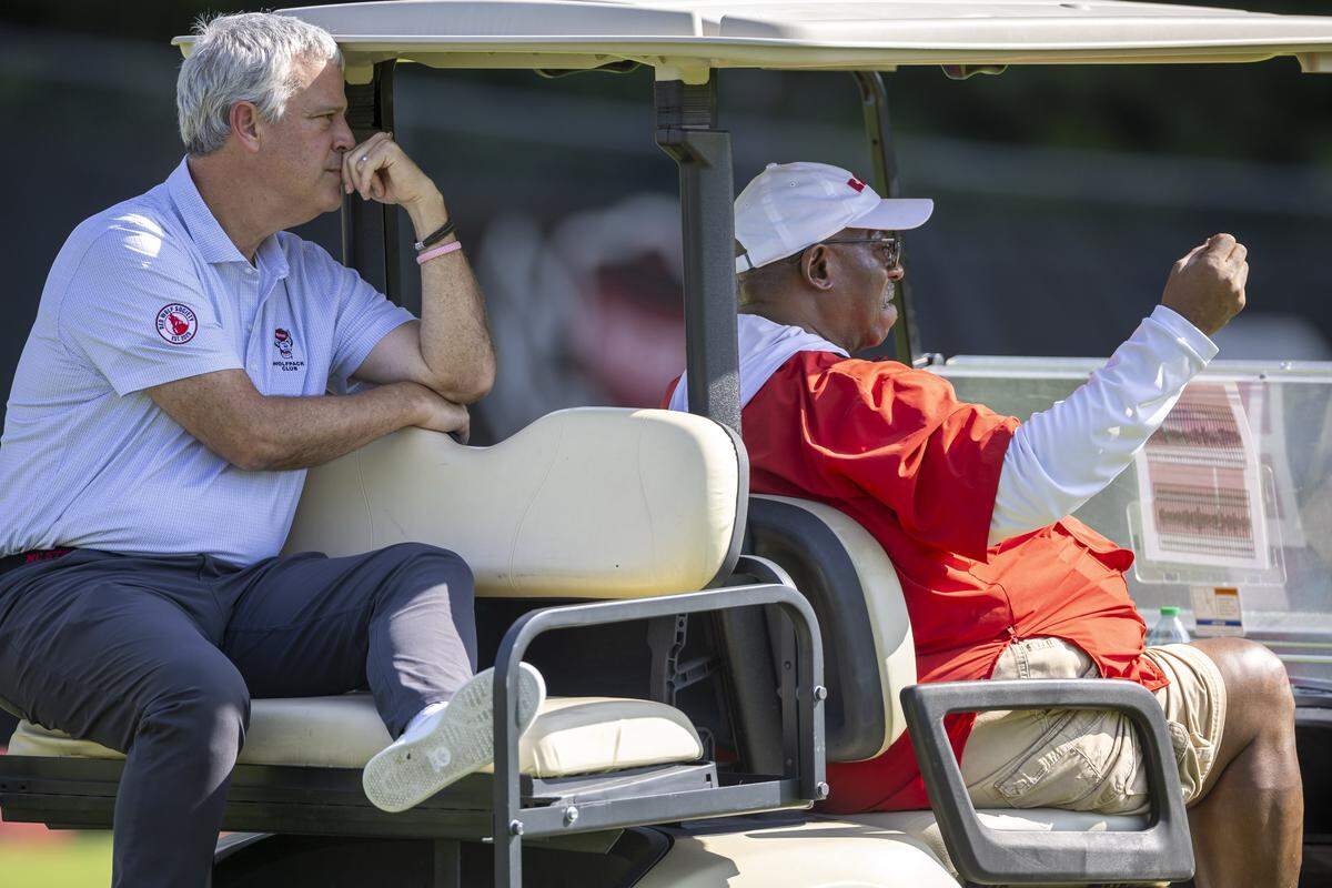 N.C. State Athletic Director Boo Corrigan watches the Wolfpack football practice from the back of a golf cart piloted by special assistant to the head coach, Ruffin McNeill on Tuesday, July 30, 2025 in Raleigh, N.C.
