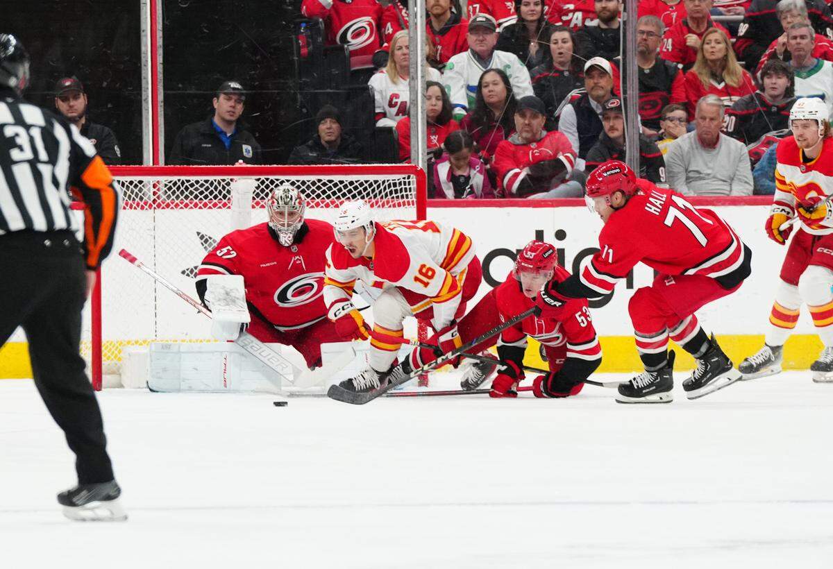 Calgary Flames center Morgan Frost (16) battles right wing Jackson Blake (53) goaltender Pyotr Kochetkov (52) and Carolina Hurricanes left wing Taylor Hall (71) for the puck during the first period at Lenovo Center.