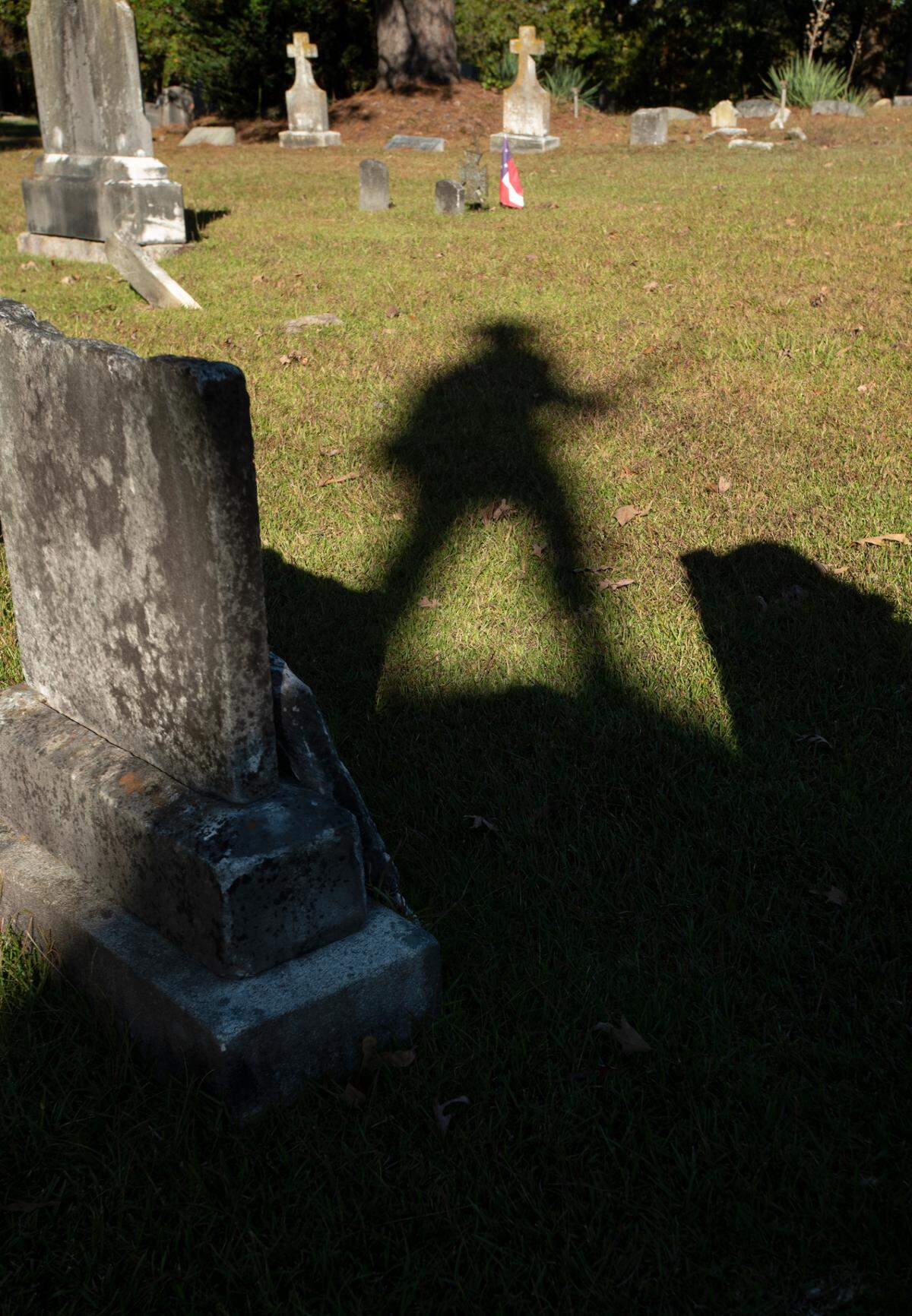 The shadow of a confederate monument falls across gravestones in the Louisburg municipal cemetery. The monument was moved to the cemetery, which contains the graves of approximately 60 confederate veterans, from its original location on Main Street in the Franklin County town.Saturday, Oct. 24, 2021.