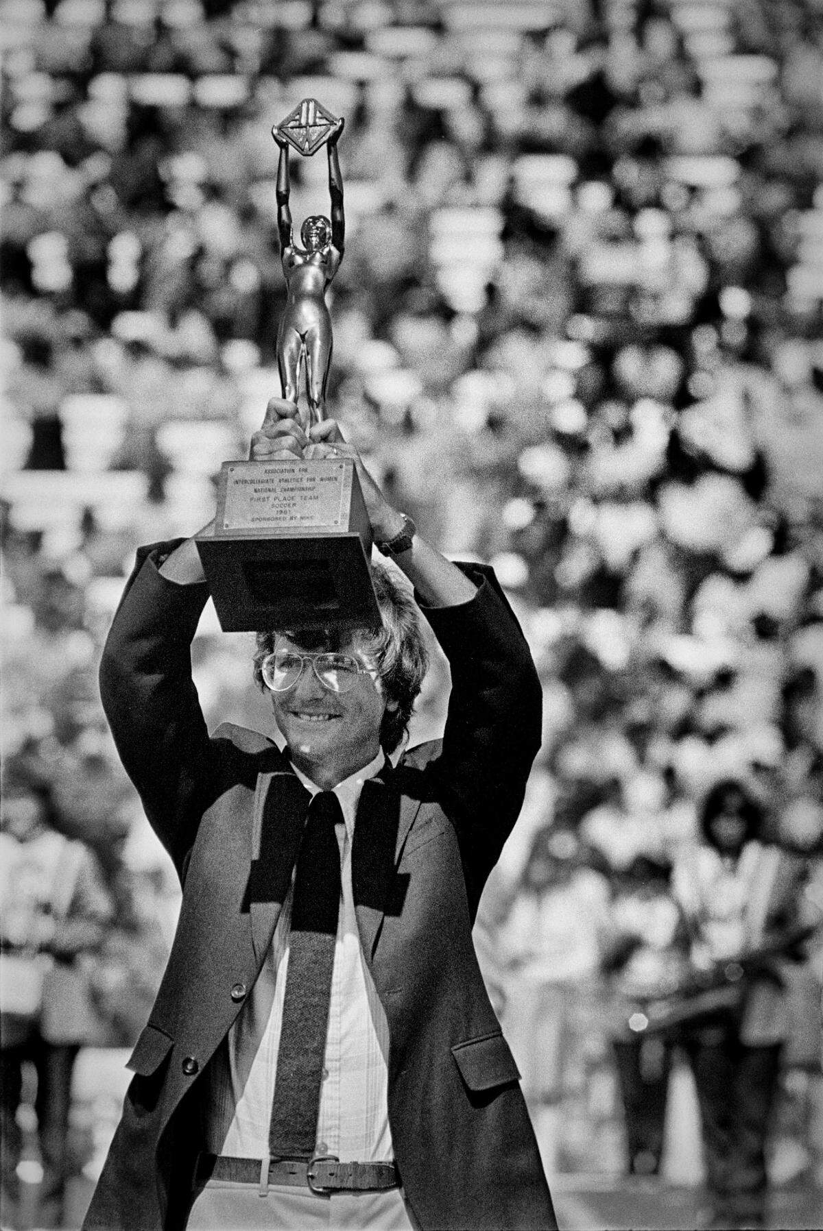 UNC women’s soccer coach Anson Dorrance holds up the 1981 NAIA National Championship trophy for the crowd at the UNC vs. Army football game in Kenan Stadium in Chapel Hill, NC Sept. 25, 1982. This was the first national championship for the team, which would become a dynasty in college women’s soccer.