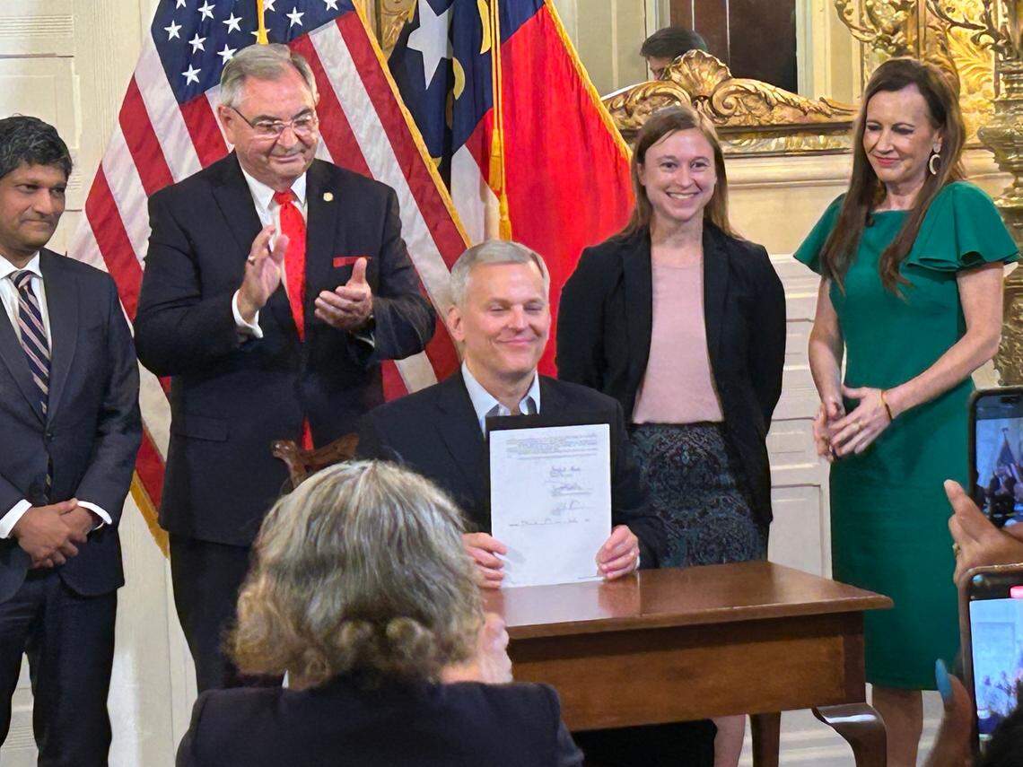 N.C. Governor Josh Stein holds up a bill he signed into law banning students from using cellphones in class. Behind him, Sen. Jay Chaudhuri, Sen. Jim Burgn, 2024 North Carolina School Counselor of the Year Annie Goldberg and Rep. Tricia Cotham applaud the bill signing held July 1, 2025 at the Executive Mansion in Raleigh. N.C.