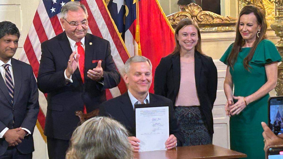 N.C. Governor Josh Stein holds up a bill he signed into law banning students from using cellphones in class. Behind him, Sen. Jay Chaudhuri, Sen. Jim Burgn, 2024 North Carolina School Counselor of the Year Annie Goldberg and Rep. Tricia Cotham applaud the bill signing held July 1, 2025 at the Executive Mansion in Raleigh. N.C.