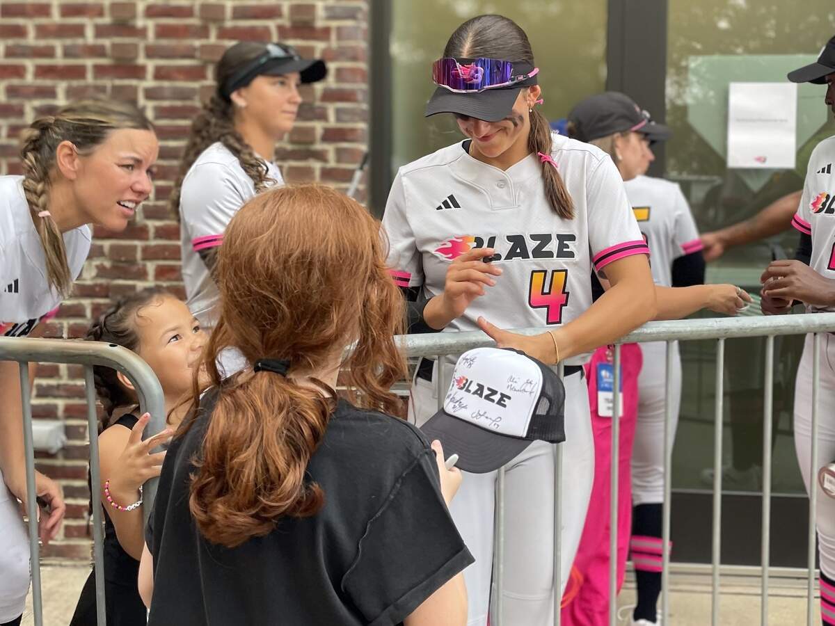 Carolina Blaze infielder Ana Gold (4) signs a softball for a fan while Keilani Ricketts (0) and her daughter, Elizabeth, look on. The Blaze defeated the Portland Cascade, 4-1, on June 9, 2026, at Smith Family Stadium in Durham, North Carolina.