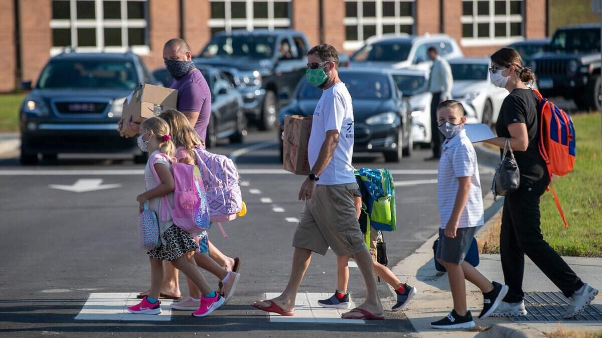 Mark Misemer, center and his daughter Jaine Misemer, a second-grader, left, walk with other families to the entrance of Thanksgiving Elementary School for the first day of classes on Monday, August 23, 2021 in Selma, N.C.