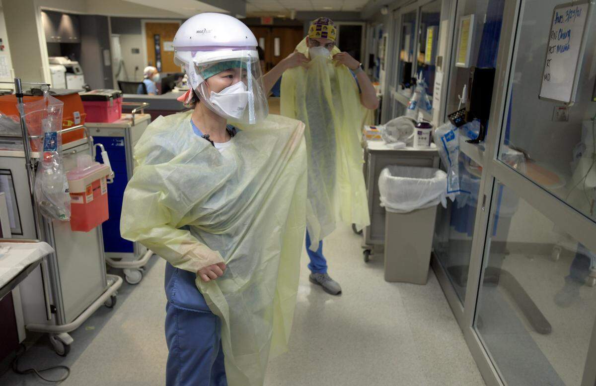 Registered nurses Qingxiao Cheng and Jonathan Vitek don protective gowns and equipment before entering a COVID patient’s room Thursday, March 25, 2021.