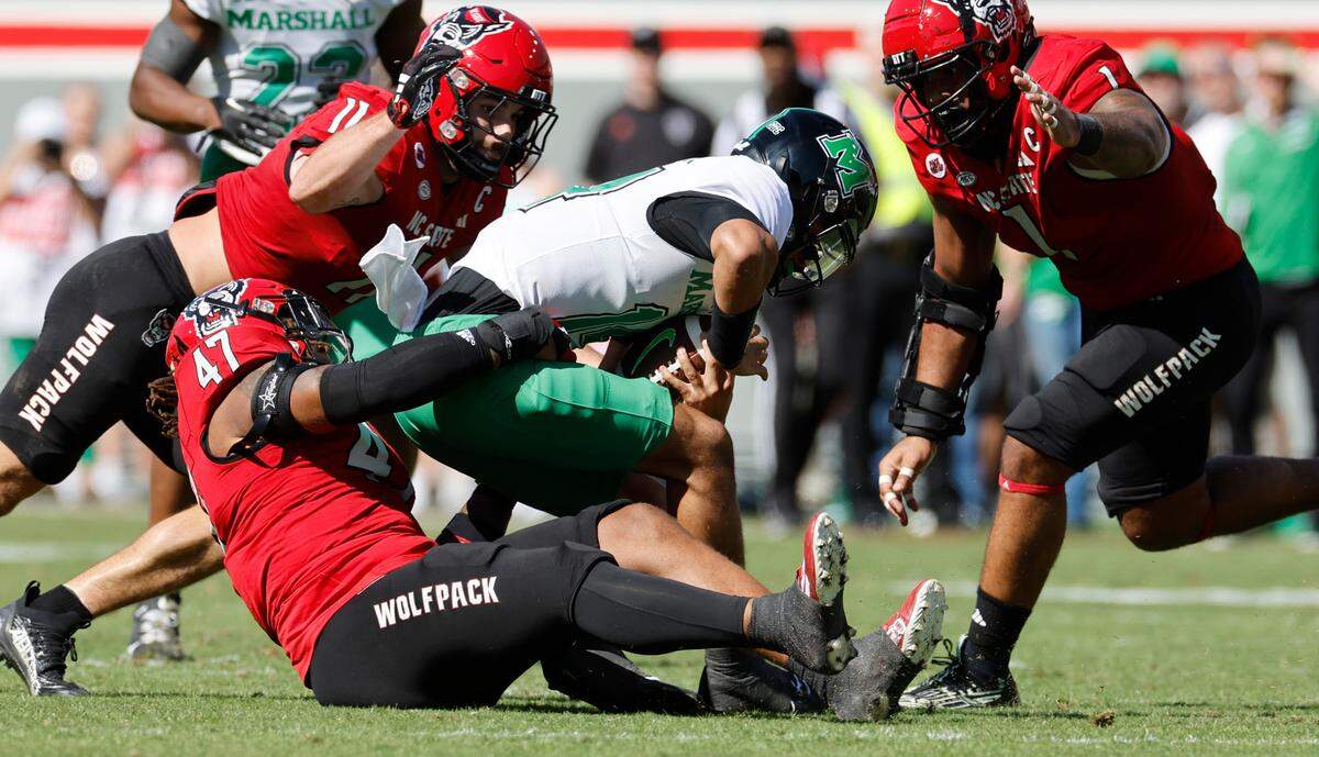 N.C. State defensive lineman Red Hibbler (47) sacks Marshall quarterback Cam Fancher (14 during the first half of N.C. State’s game against Marshall at Carter-Finley Stadium in Raleigh, N.C., Saturday, Oct. 7, 2023. N.C. State linebacker Payton Wilson (11) and defensive tackle Davin Vann (1) also close in.