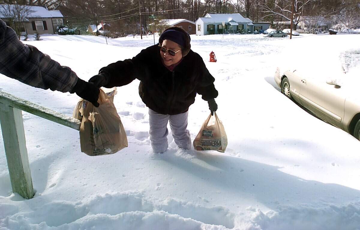Brenda Davis gets a  helping hand from her husband David as they return from a trip to the grocery store through knee-deep snow in 2000.