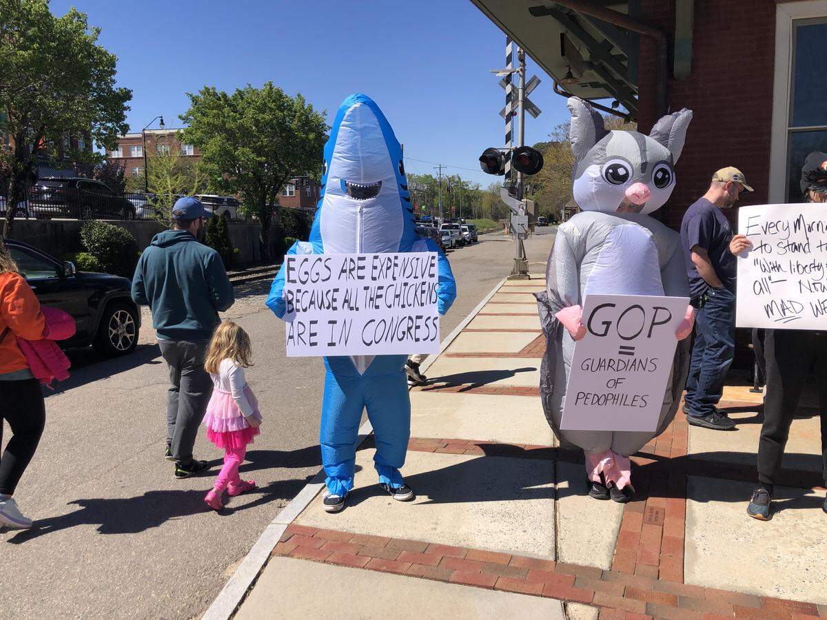 A protester in a shark costume at the “No Kings” rally in Sanford on March 28 holds up a sign that says, “Eggs are expensive because all the chickens are in Congress.”