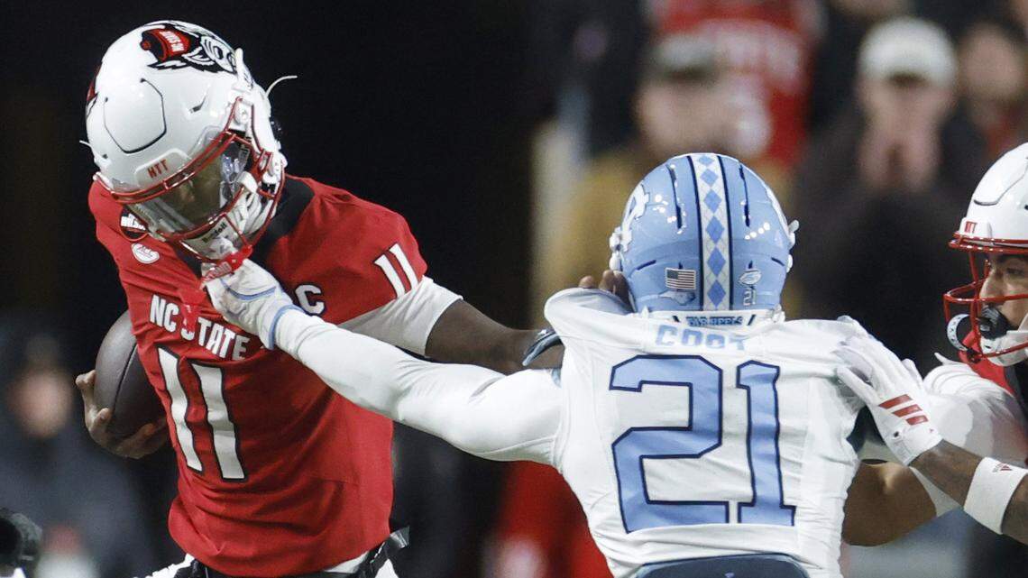 North Carolina’s Kaleb Cost (21) pulls the face mask of N.C. State quarterback CJ Bailey (11) during the first half of N.C. State’s game against UNC at Carter-Finley Stadium in Raleigh, N.C., Saturday, Nov. 29, 2025.