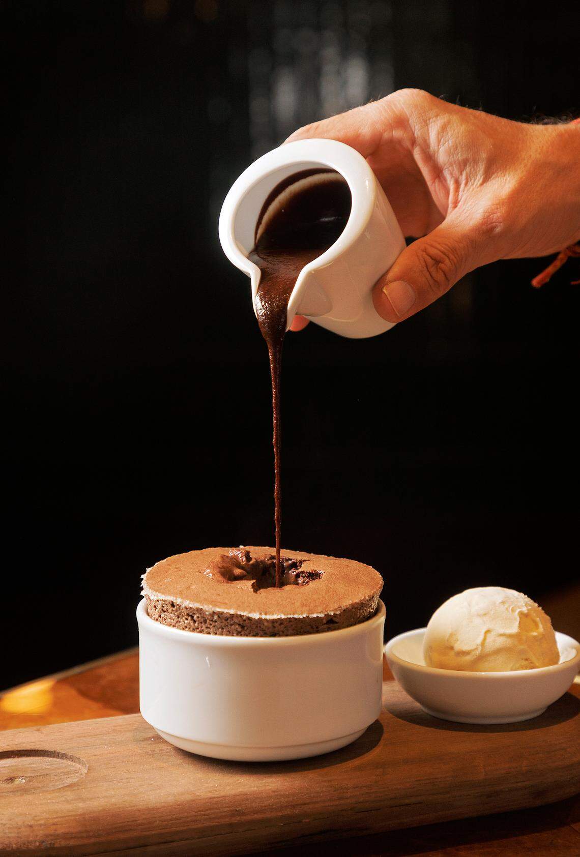 Hot fudge is poured into a hot chocolate soufflé, served alongside bourbon caramel ice cream at Nanas on Wednesday, Nov. 22, 2023, in Durham, N.C.