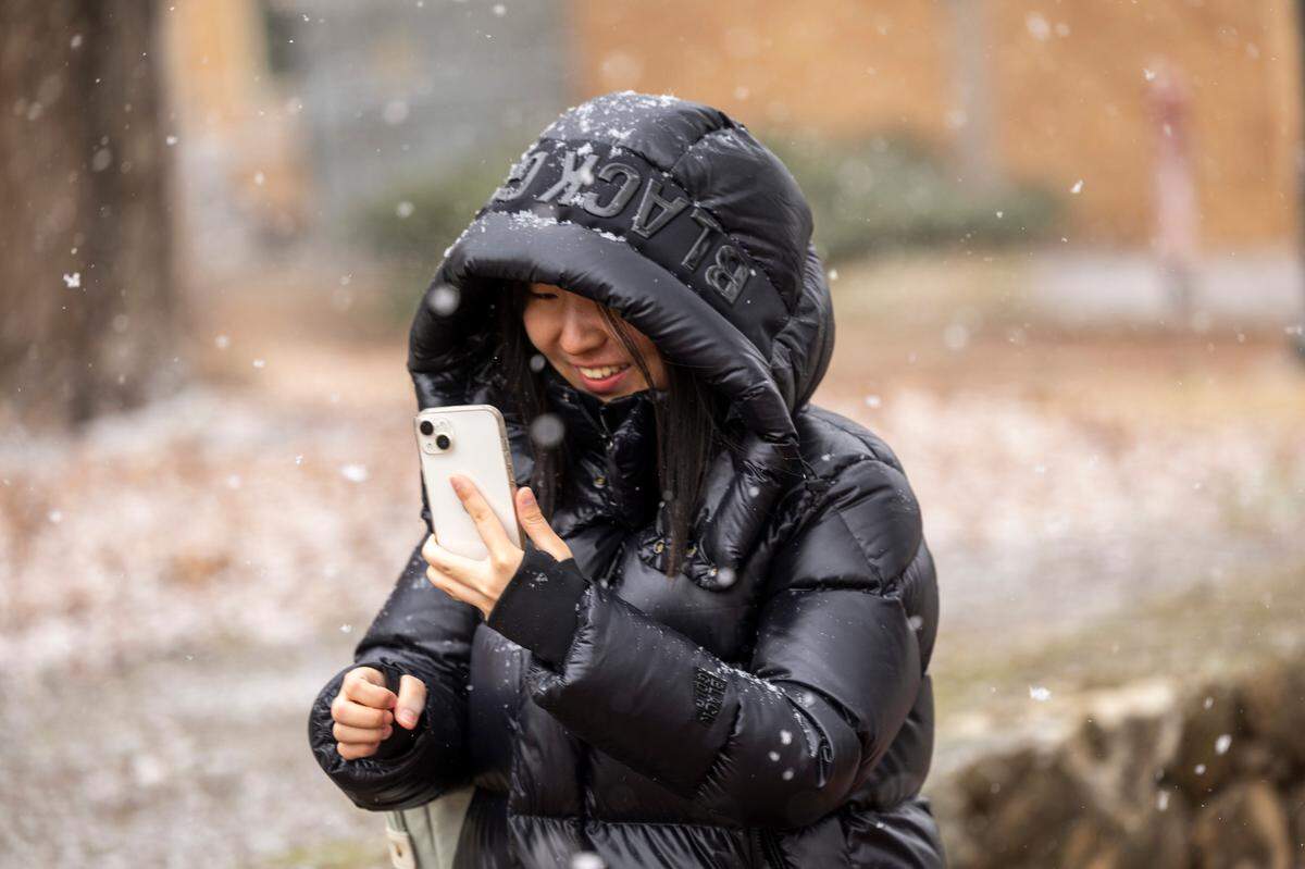 A woman who did not want to be identified by name makes photographs with her phone as snow begins to fall near UNC-Chapel Hill on Wednesday, Feb. 19, 2024.