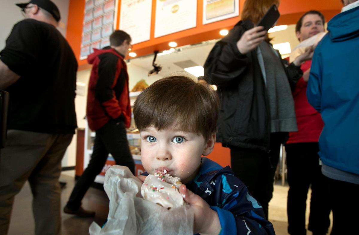 Patrons, like Ross Mize, 2, of Chapel Hill, gets his first taste of a Rise donut who lined up around the building in light rain for their first tastes of donuts at a free giveaway at Rise-Carrboro on Tuesday, February 23, 2016 from 12-2pm.