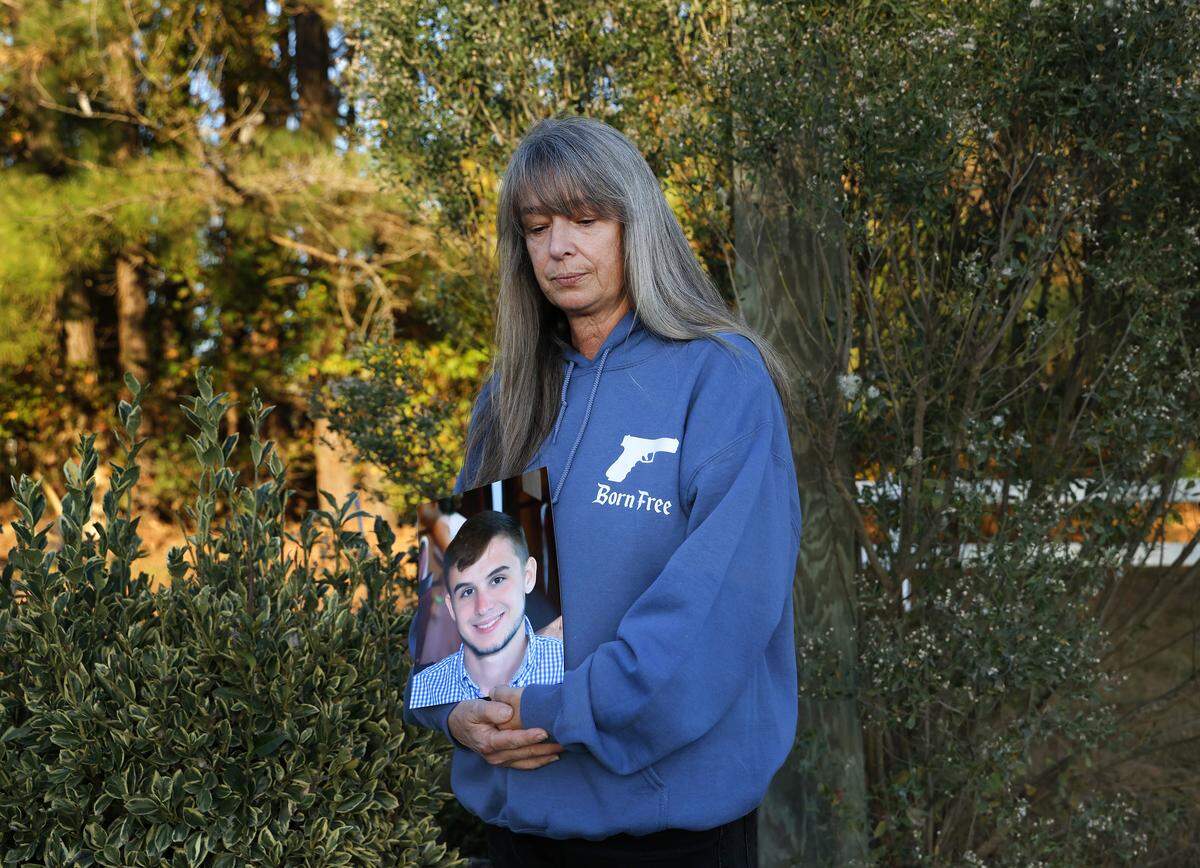 Lisa Higgins holds a photograph of her son, Michael Higgins, while standing next to his roadside memorial in November. Michael, a Highway Patrol intern, died after a trooper reached 113 mph and lost control of his patrol car on a rural Pitt County road in August 2020.