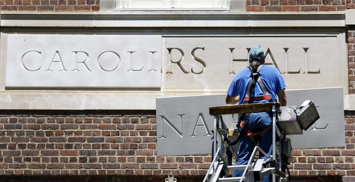 Sign installer Roger Phillips of Broach Custom Signs in Wendell, NC slowly rises with the second urethane panel of the new Carolina Hall nameplate Thursday afternoon, August 13, 2015 to cover the old Saunders Hall name on the UNC-CH campus. After an outcry over the personal history of the 19th century UNC alumnus William L. Saunders the university decided recently to change the name to Carolina Hall, removing all vestiges of the old name.