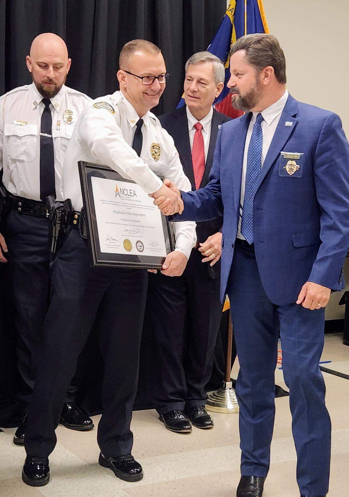 Knightdale Police Chief Lawrence Capps holds a North Carolina Law Enforcement Accreditation plaque and shakes someone’s hand.