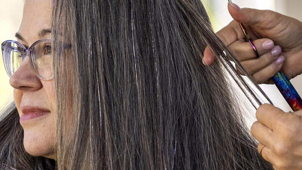 Leslie Stern applies fairy hair, metallic-like threads of tinsel, to her friend Liz Buno’s hair without compensation as a personal arrangement at Stern’s home in Durham on Thursday, March 19, 2026. It is unclear whether regulators with the North Carolina Board of Cosmetic Art Examiners require a natural hair care certification and a licensed shop for artists like Stern to provide fairy hair services.