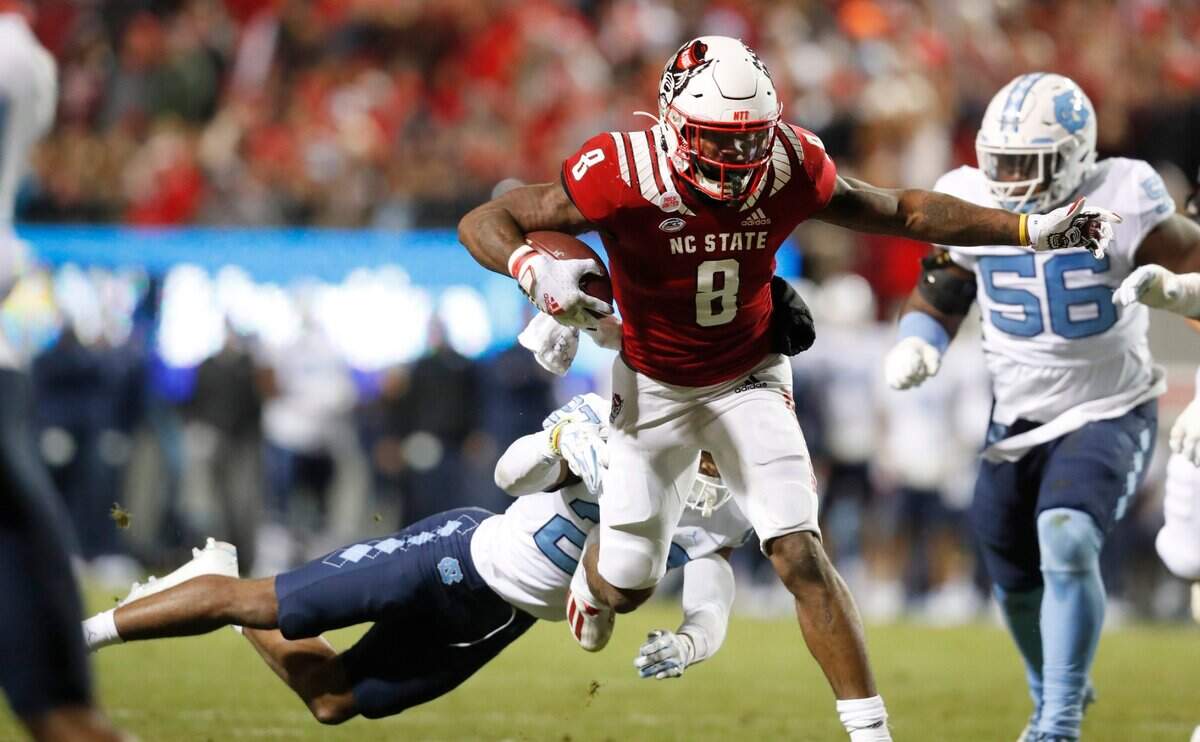 N.C. State running back Ricky Person Jr. (8) escapes the tackle by North Carolinas Giovanni Biggers (27) during the first half of N.C. States game against UNC at Carter-Finley Stadium in Raleigh, N.C., Friday, November 26, 2021.