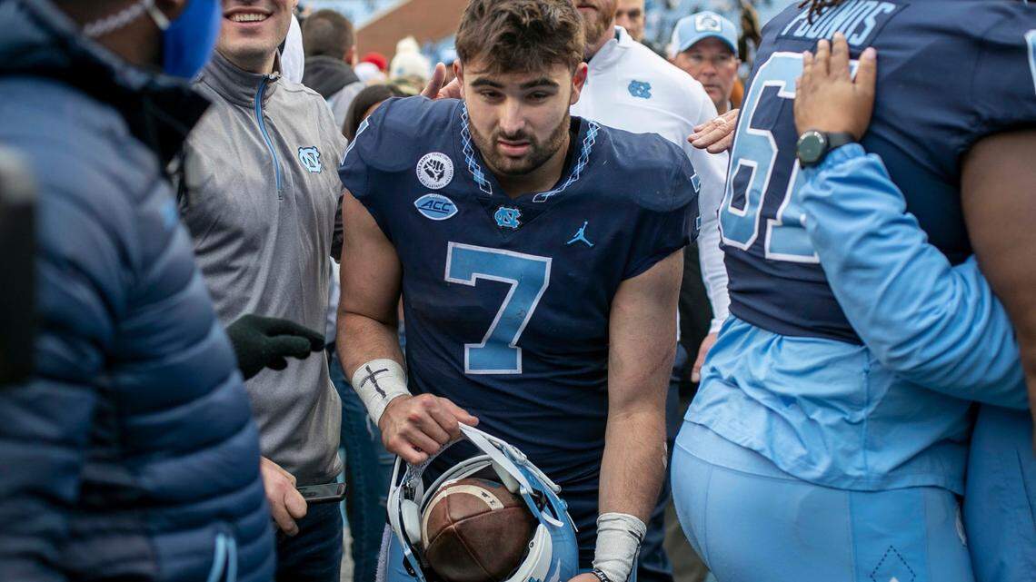 North Carolina quarterback Sam Howell (7), carrying a game ball in his helmet, works his way through fans that stormed the field, following the Tar Heels’ 58-55 victory over Wake Forest on Saturday, November 6, 2021 at Kenan Stadium in Chapel Hill, N.C.