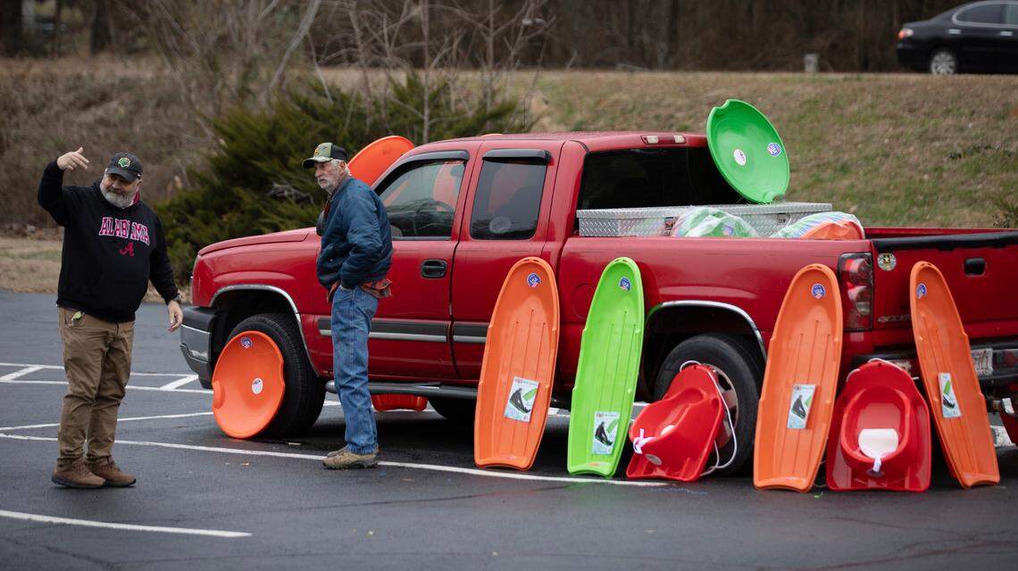 Motion for several of his Mike Fann (left) children to come pick out sleds being sold by Johnny Howard in a parking lot in Pittsboro, Friday, January 10, 2025.
