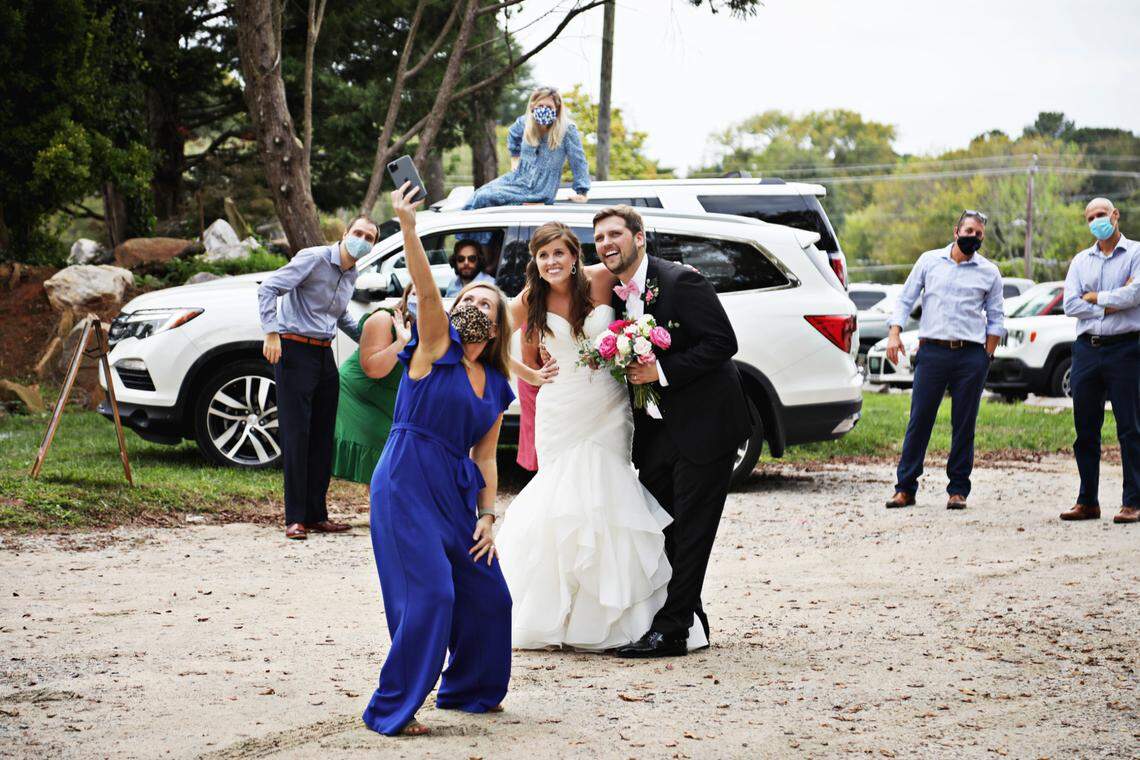 Carrie and John Michael Simpson, center, take socially-distanced selfies with guests after their wedding ceremony on Sunday, Sept. 27, 2020, in Youngsville. The couple decided to have their ceremony in the parking lot of the Victorian House so that they could invite more guests who could watch from their cars.