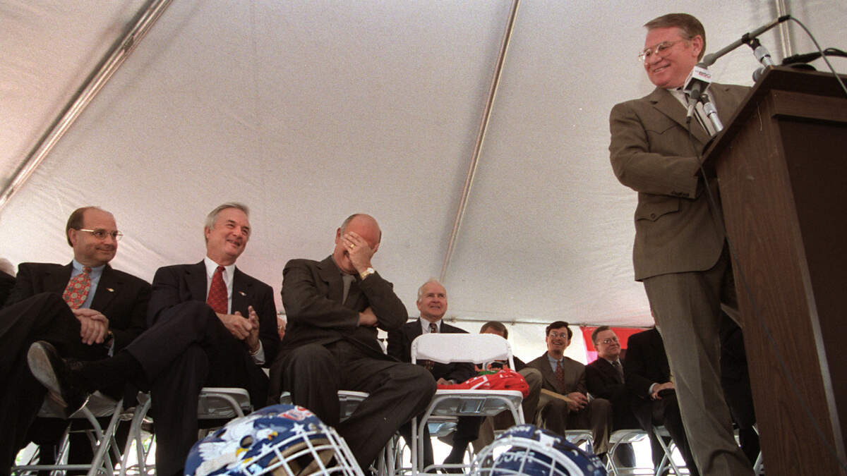 Hartford Whalers owner Peter Karmanos (center) reacts to a joke by Steve Stroud (podium) about a Stanley Cup playoff game being held soon in the new arena during 1997 ceremonies announcing that the Whalers will move to Raleigh. From left: Speaker of the N.C. House of Representatives Harold Brubaker, Governor Jim Hunt, Karmanos, and Stroud.