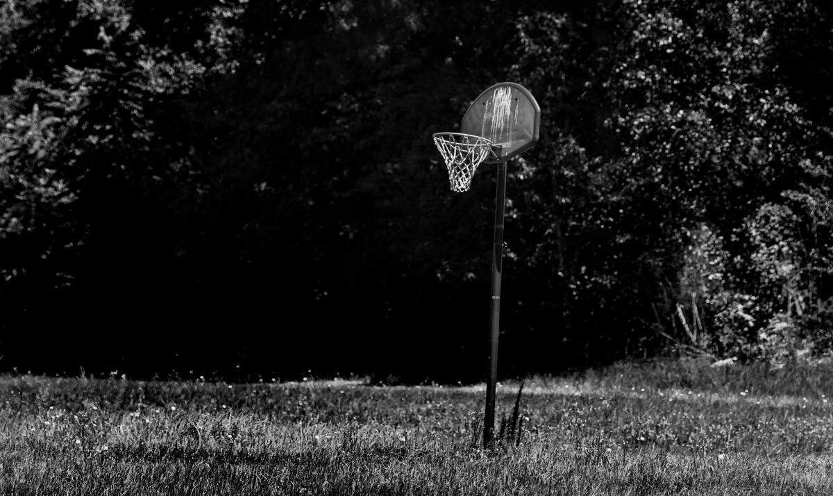 A lonely basketball goal stands in a field in eastern North Carolina, grass having grown over the dirt court.