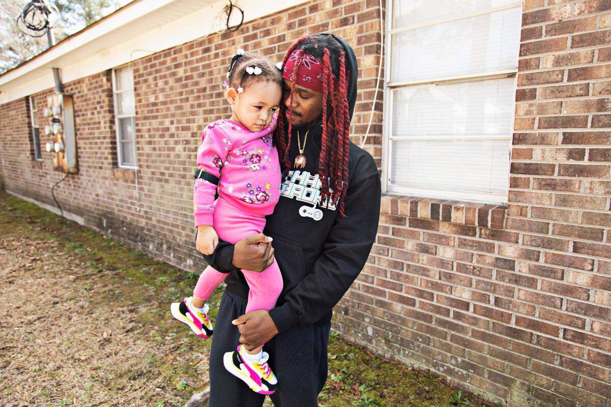 Sedriq Crandell, right, nuzzles his two-year-old daughter, Emerald, outside of their Rocky Mount home on Thursday, March 3, 2022. Crandell, who worked at QVC for four years and escaped the fire along with several co-workers, has not been able to find a comparable job since the fire.