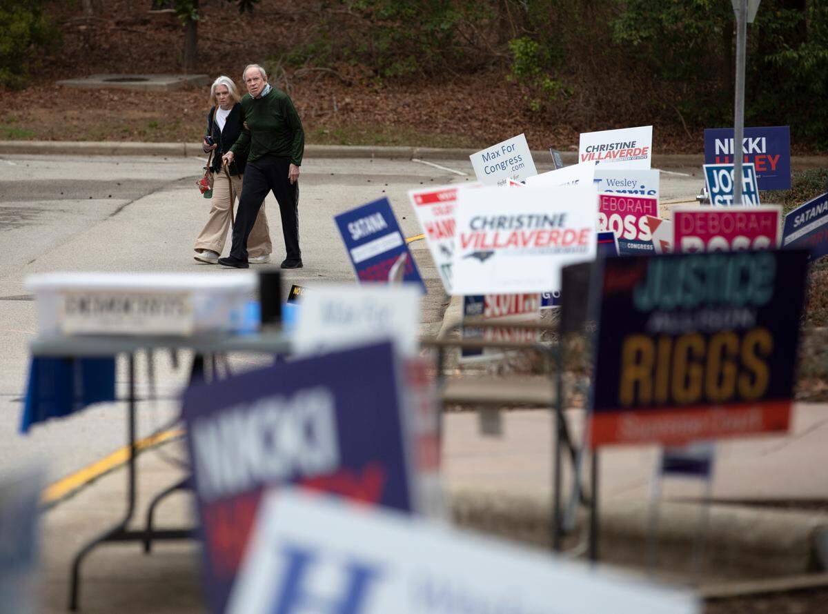 People walk by campaign signs outside of a voting location at the Herbert C. Young Community Center in Cary, N.C. on Tuesday, March 5, 2024.