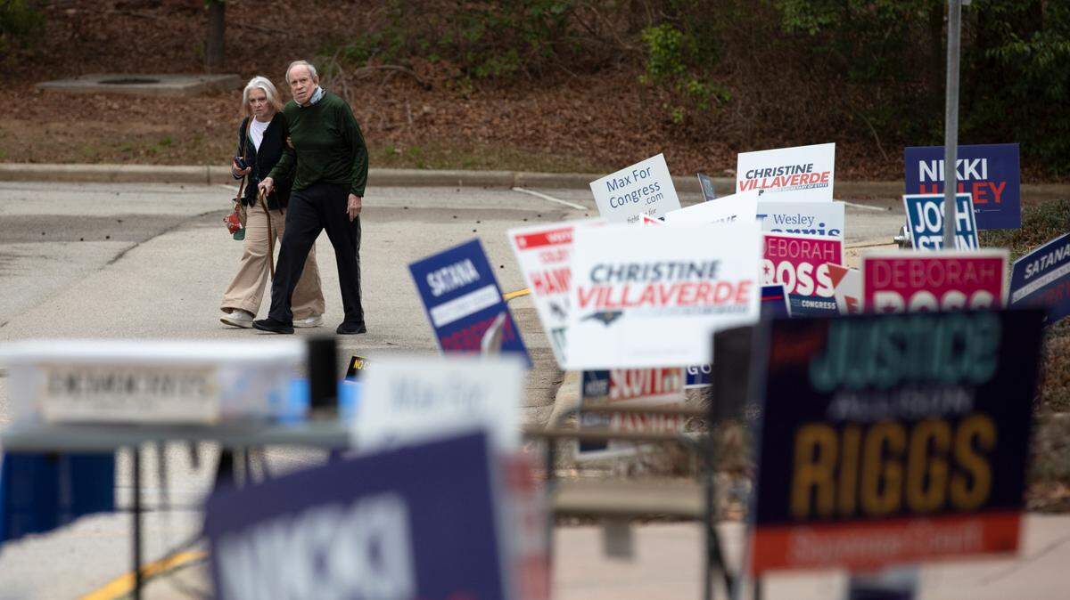 People walk by campaign signs outside of a voting location at the Herbert C. Young Community Center in Cary, N.C. on Tuesday, March 5, 2024.