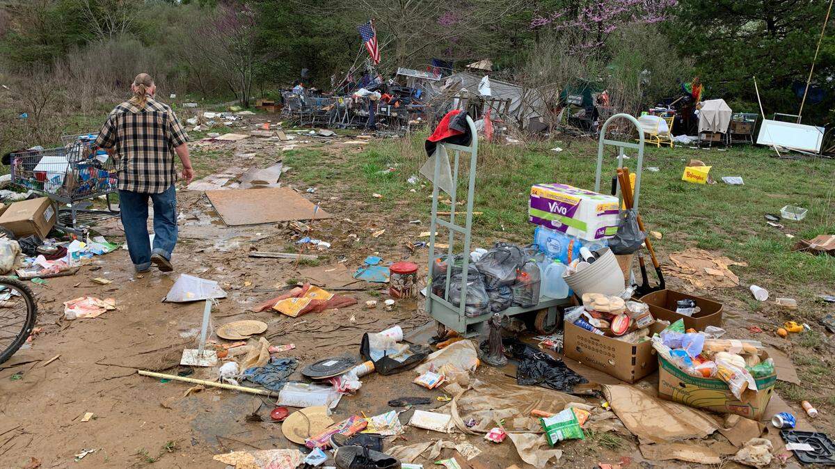 Michael Kelly, a street outreach specialist for Triangle Family Services, walks along the edge of a homeless camp off Capital Boulevard and Interstate 540 on Friday. In the foreground are shovels, rakes and other cleaning supplies that residents and volunteers will use to begin cleaning up the site.