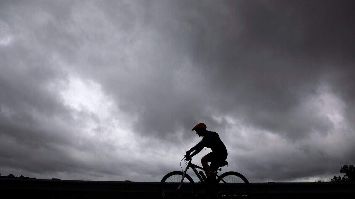 Travis James rides a bicycle near Falls Lake Dam as storm clouds from approaching Tropical Storm Debby fill the sky on Wednesday, Aug. 7, 2024, in Raleigh, N.C.