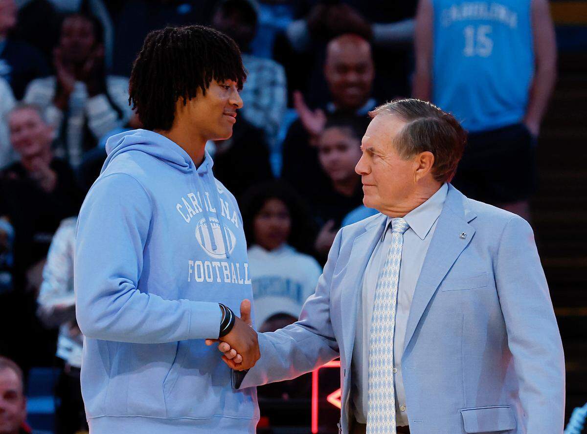 North Carolina football recruit Bryce Baker shakes hands with recently hired football coach Bill Belichick as they are introduced during halftime of the Tar Heels’ men’s basketball game against La Salle on Saturday, Dec. 14, 2024, at the Smith Center in Chapel Hill, N.C.