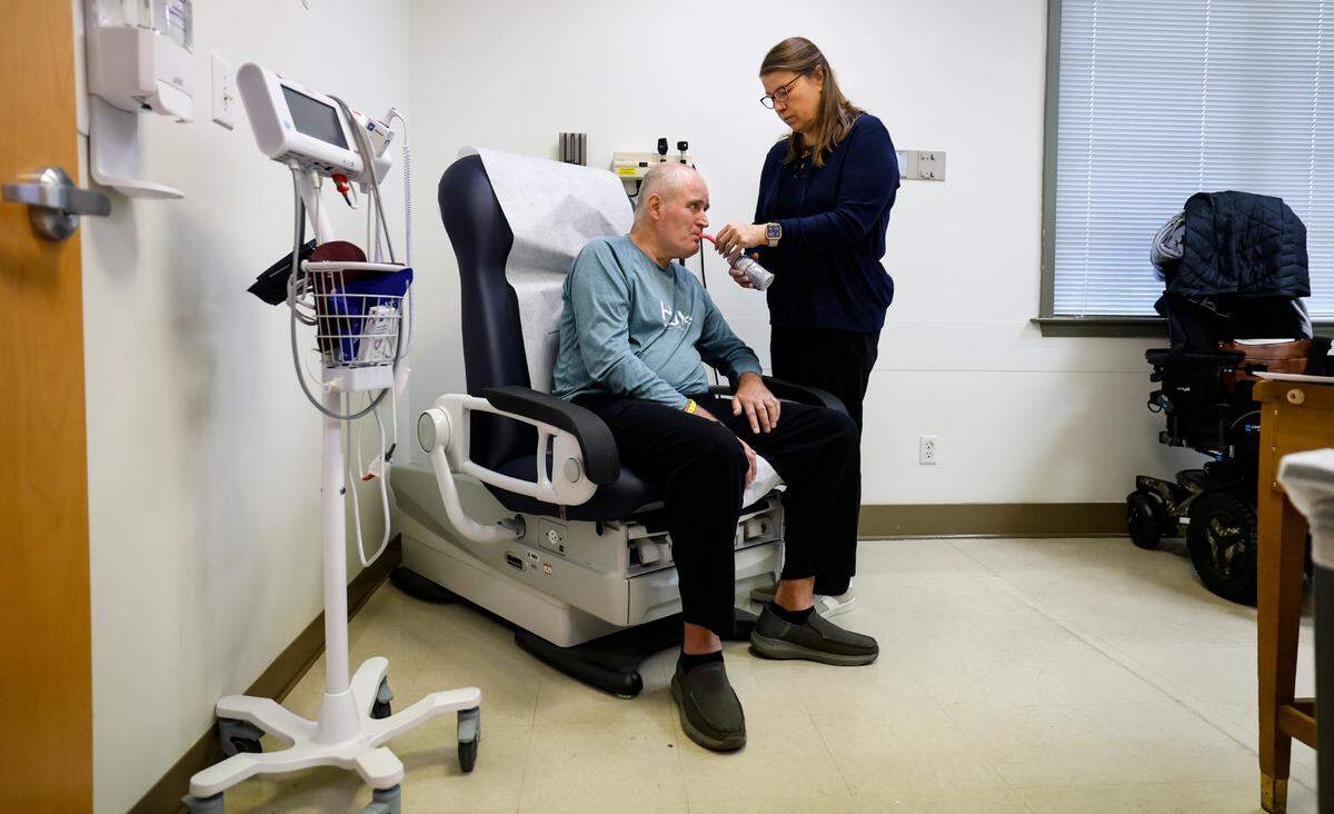 Jamie Woodlief feeds her husband Roy an Ensure nutritional shake during his appointment at the Duke ALS Clinic in Durham, N.C., Tuesday, Jan. 21, 2025. Roy has been diagnosed with amyotrophic lateral sclerosis (ALS), forcing him to retire from the Wake County Sheriff’s Office. The fatal disease causes muscle weakness, making it difficult to walk, eat and eventually breathe.