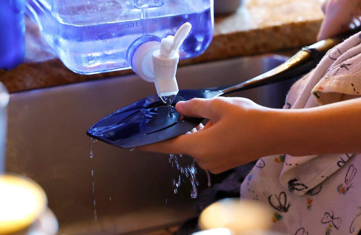 Paul Bloemendaal, 13, washes utensils with water from a two gallon container in their home in Banner Elk, N.C., Wednesday, Oct. 9, 2024. The Bloemendaal’s power has been restored but there is no estimate on when they will get water back.