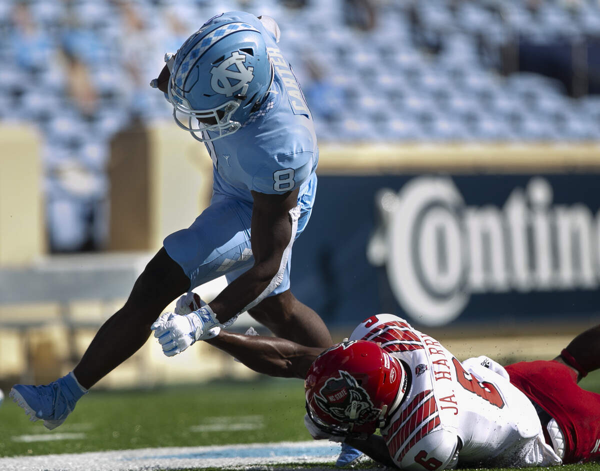 North Carolina’s Michael Carter (8) scores on a 16 yard rush in the first quarter ahead of N.C. State’s Jakeen Harris (6) to give the Tar Heels’ a 7-0 lead at Kenan Stadium on Saturday, October 24, 2020 in Chapel Hill, N.C.