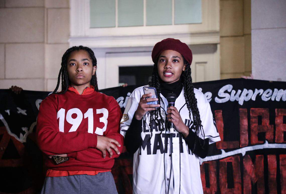 UNC Black Student Movement president, Qieara Lesesne, left, listens as Alex Robinson, vice president, speaks to a large crowd gathered at Peace and Justice Plaza in Chapel Hill, N.C. on Monday, Dec. 3, 2018.