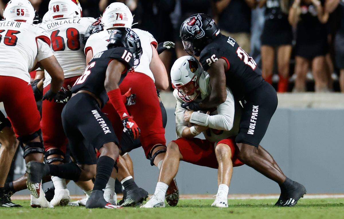 N.C. State safety Rakeim Ashford (16) and N.C. State linebacker Devon Betty (26) tackle Louisville quarterback Jack Plummer (13) for a loss during the second half of Louisville’s 13-10 victory over N.C. State at Carter-Finley Stadium in Raleigh, N.C., Friday, Sept. 29, 2023.
