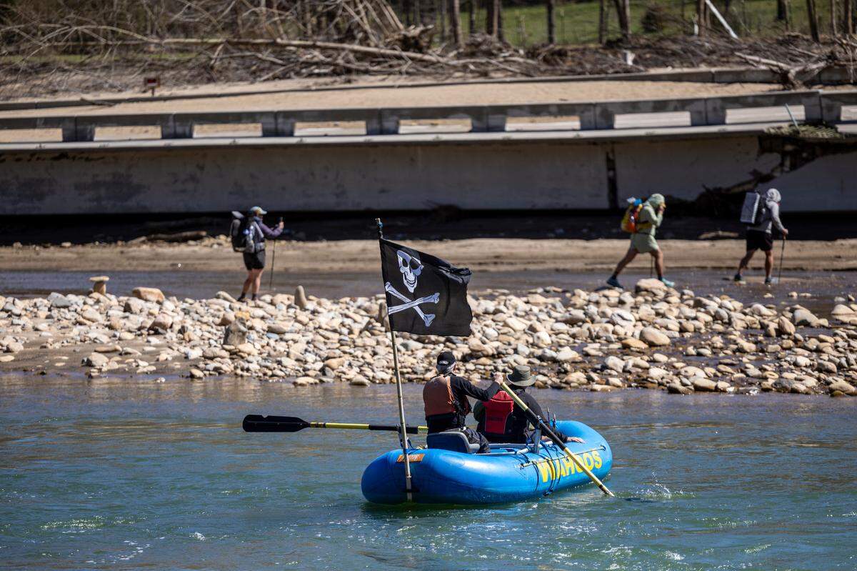 A section of the washed-out Chestoa Pike Bridge is visible in the background as Mike Crooks ferries an Appalachian Trail hiker known as “Tie-Dye” across the Nolichucky River in Erwin, Tennessee.