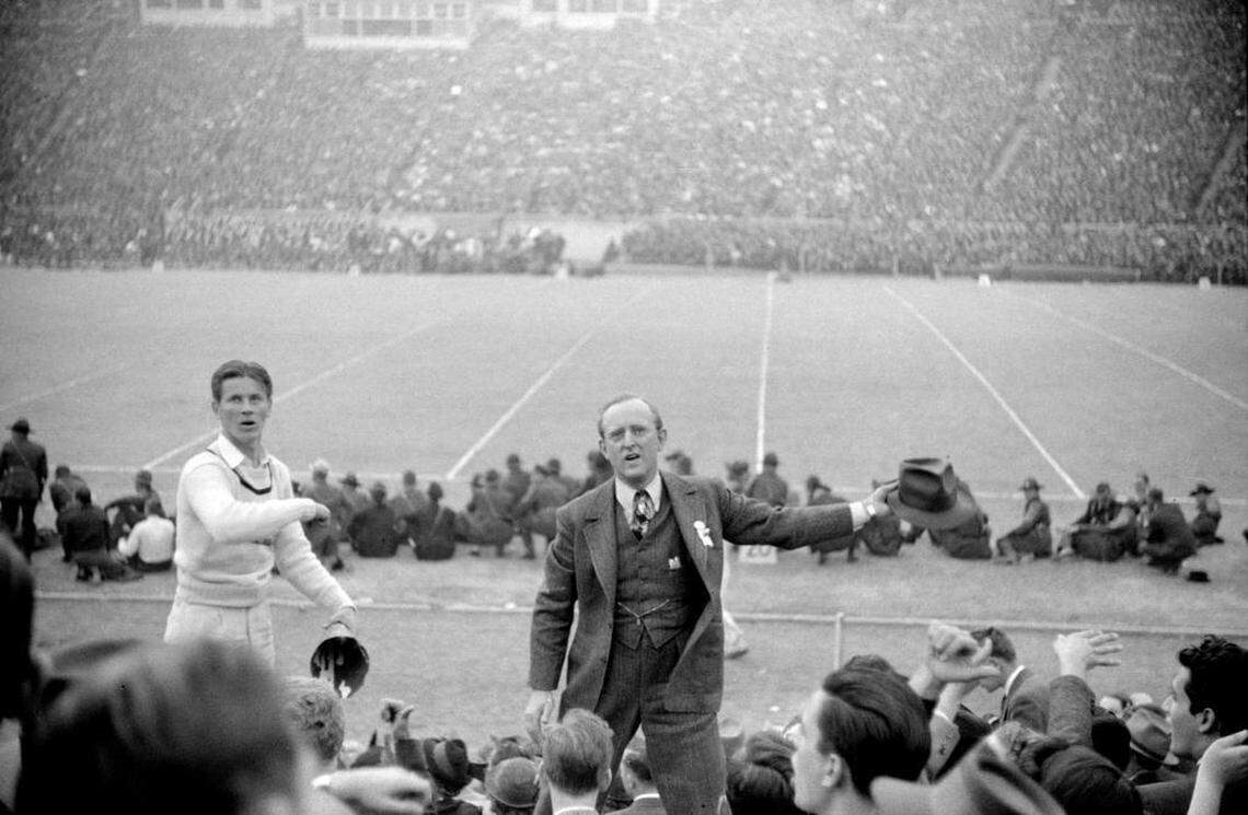 Fans ringed the sidelines and famous bandleader Kay Kyser (right) and a UNC cheerleader lead the crowd in cheers at the 1939 Duke-Carolina game played in Durham, NC.