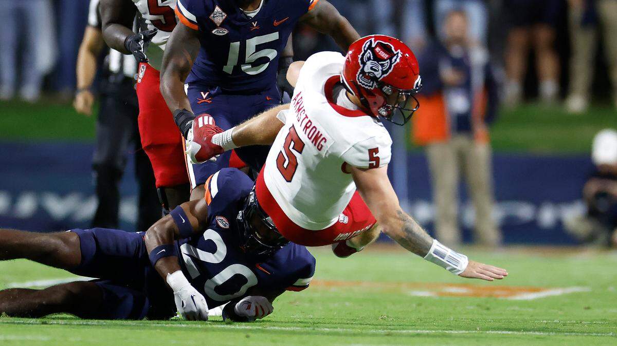 N.C. State quarterback Brennan Armstrong (5) gets tripped up by Virginia safety Jonas Sanker (20) during the first half of N.C. State’s game against Virginia at Scott Stadium in Charlottesville, Va., Friday, Sept. 22, 2023.