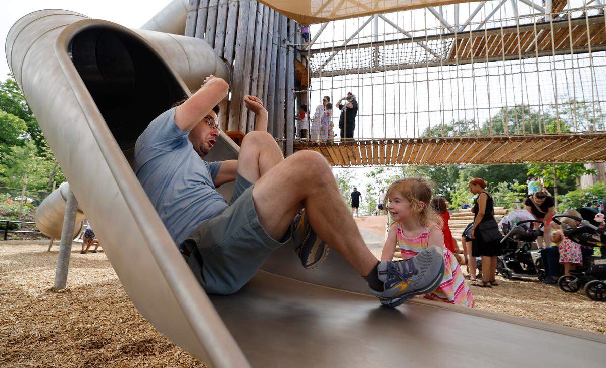 As his daughter Lily, 3, watches, Michael Brenneis emerges from a slide at Gipson Play Plaza at Dix Park during a preview day Saturday, May 24, 2025. The park will officially open with a grand opening celebration on June 6th, 7th and 8th.