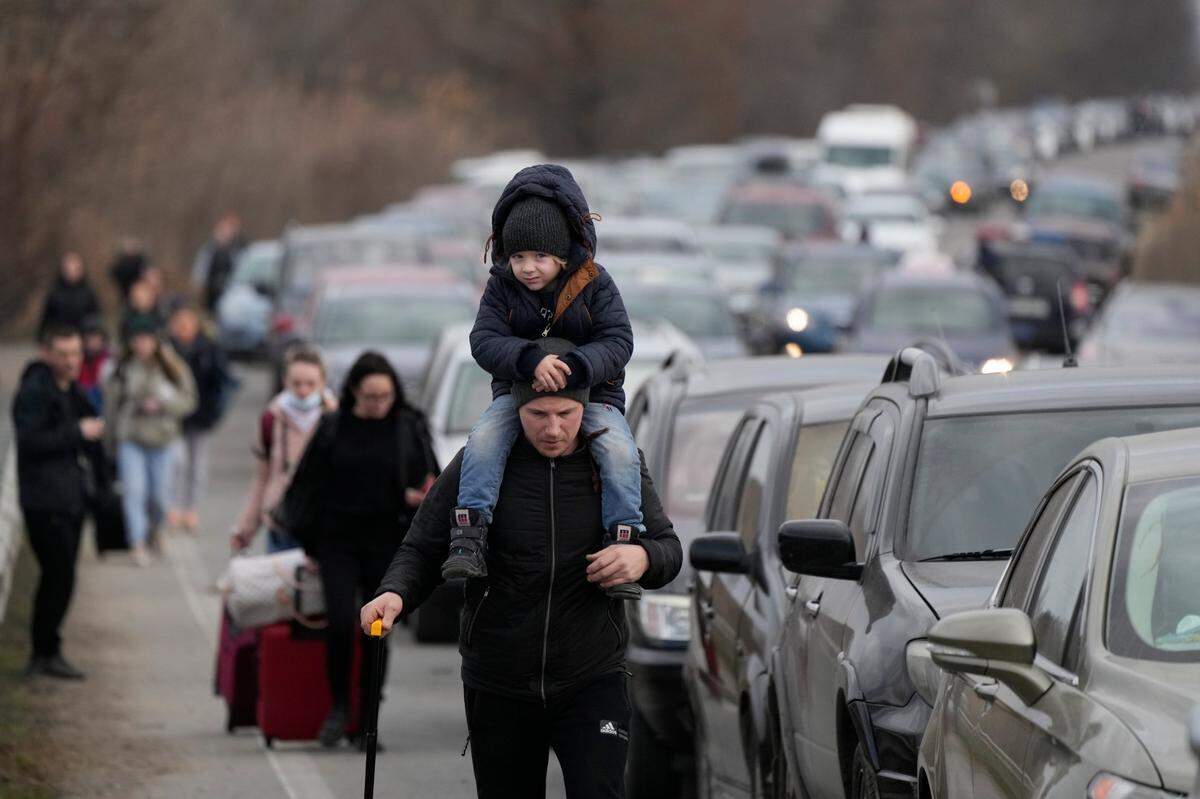 Ukrainian refugees walk along vehicles lining-up to cross the border from Ukraine into Moldova, at Mayaky-Udobne crossing border point near Mayaky-Udobne, Ukraine, Saturday, Feb. 26, 2022. The U.N. refugee agency says nearly 120,000 people have so far fled Ukraine into neighboring countries in the wake of the Russian invasion. The number was going up fast as Ukrainians grabbed their belongings and rushed to escape from a deadly Russian onslaught.