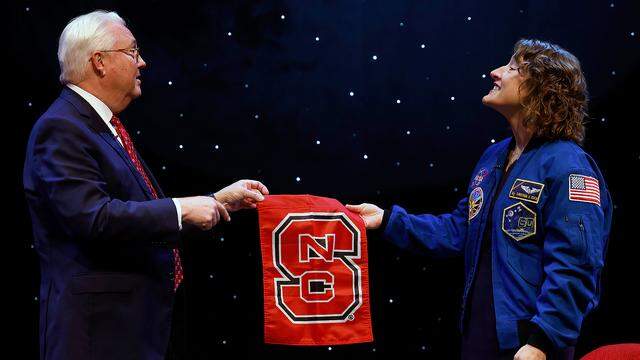 Christina Koch, a NASA astronaut and NC State alumna, shows Chancellor Randy Woodson an NC State flag that she took with her to space during an event on Monday, Oct. 23, 2023, in Talley Student Union’s Stewart Theater. In December 2019, Koch broke the world record for the longest spaceflight by a woman, going on to spend more than 300 days in orbit. 