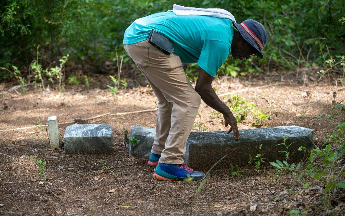 James Rankin examines a fallen grave stone in the Wilkins Cemetery on Wednesday, August 24, 2022 in Dunn, N.C.