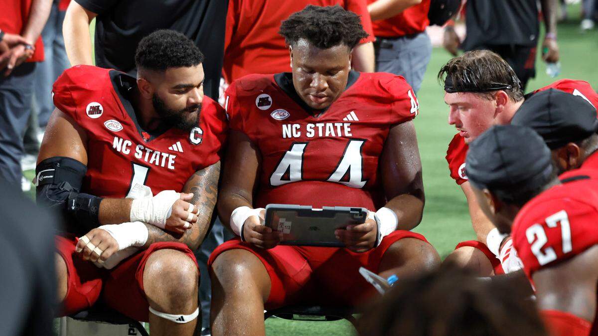 N.C. State’s Davin Vann (1), Brandon Cleveland (44) and Noah Potter (97) look over a tablet during the Wolfpack’s 38-21 victory over Western Carolina at Carter-Finley Stadium in Raleigh, N.C., Thursday, August 29, 2024. The Wolfpack are scheduled to play the Tennessee Volunteers Sept. 7, a game that local DirecTV customers may not be able to watch at home due to the carrier’s contract dispute with Disney.