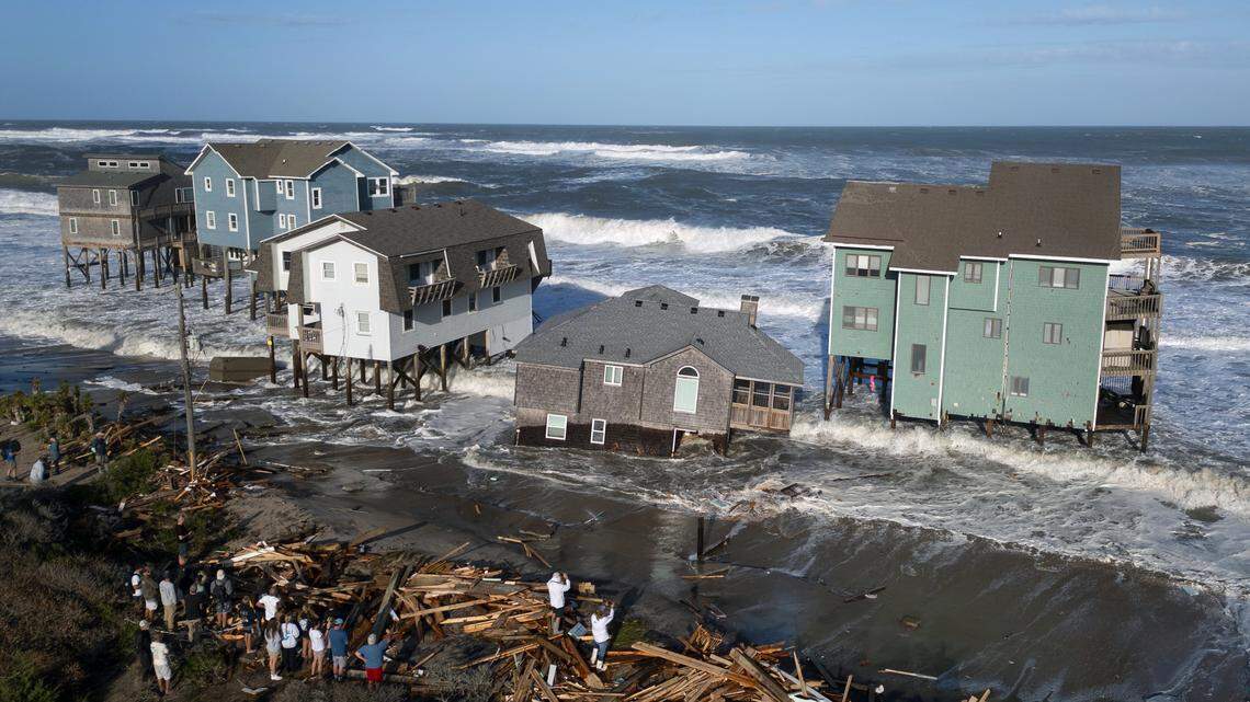 Onlookers view houses surrounded by crashing waves as one collapses into the surf in Buxton on the N.C. Outer Banks on Thursday, Oct. 2, 2025.